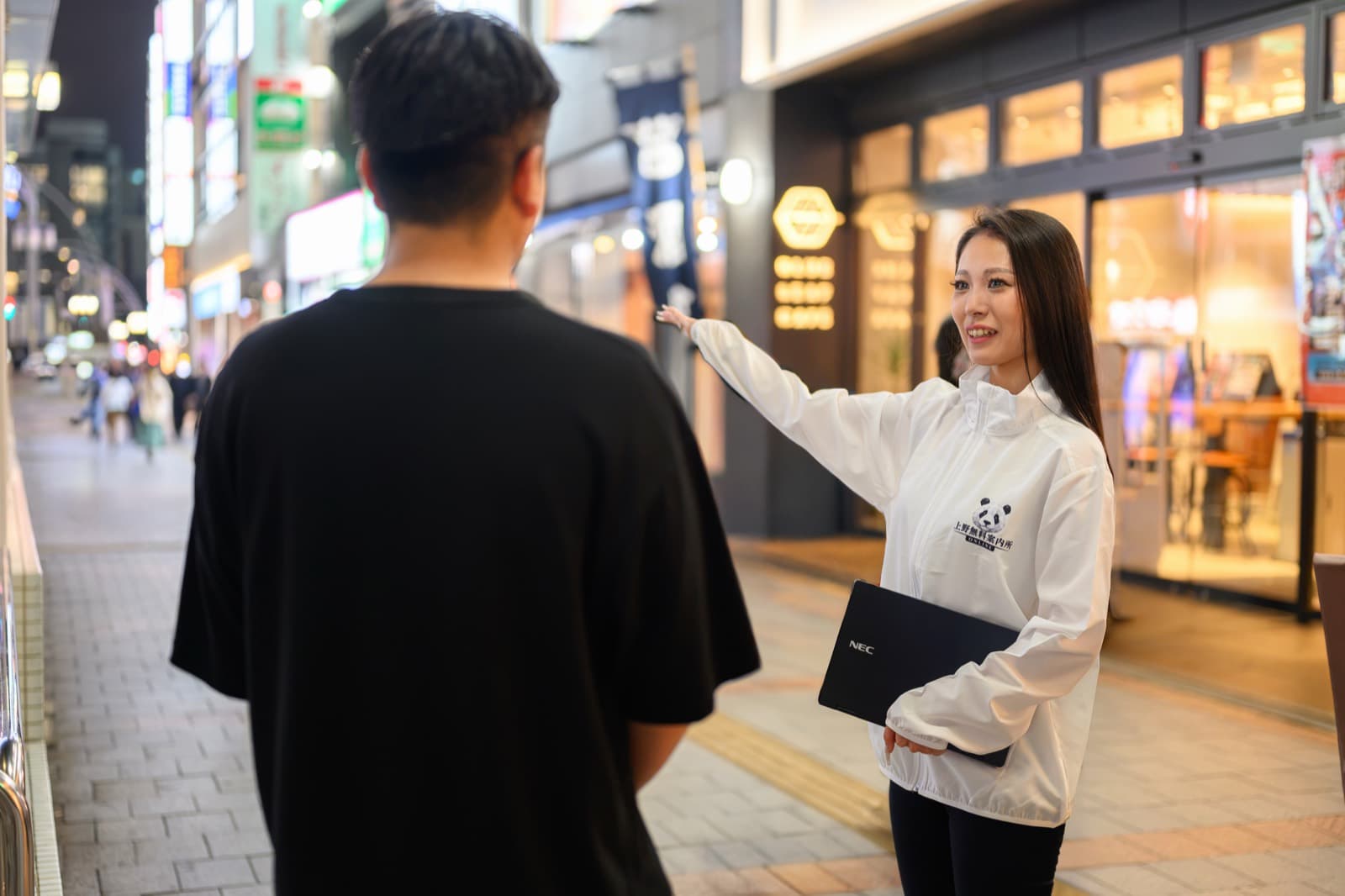 夜の上野の街で待ち合わせ場所からお客様をお店までお迎え・ご案内する上野オンライン無料案内所の女性スタッフ