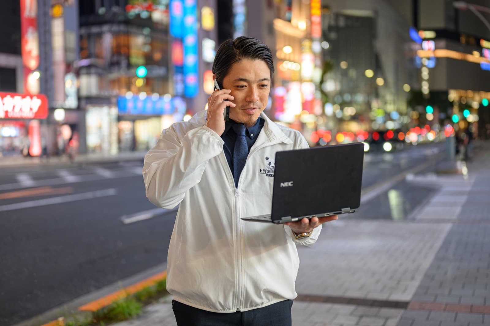 夜の上野の街でノートパソコンを手にお客様をお店の入口まで案内する男性の案内スタッフ