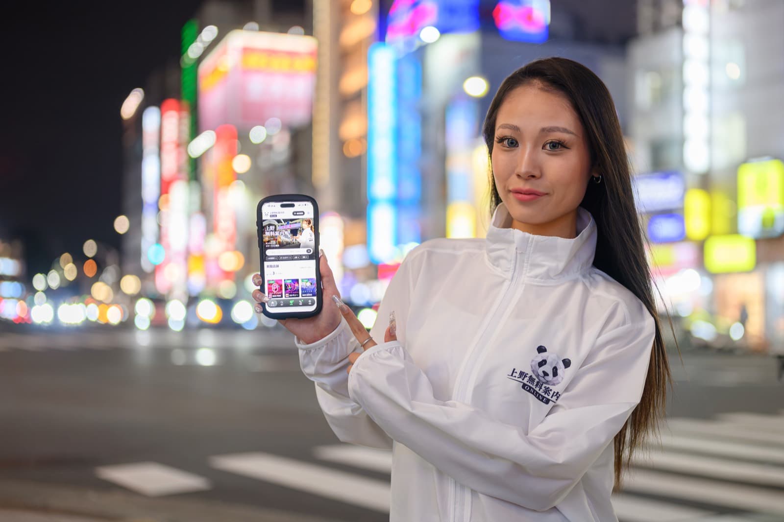 夜の上野の街でスマートフォンを手に LINE 相談を案内する女性の案内スタッフ